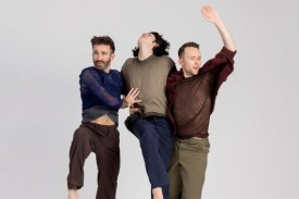 3 dancers jumping while connected side-to-side in front of a grey background.